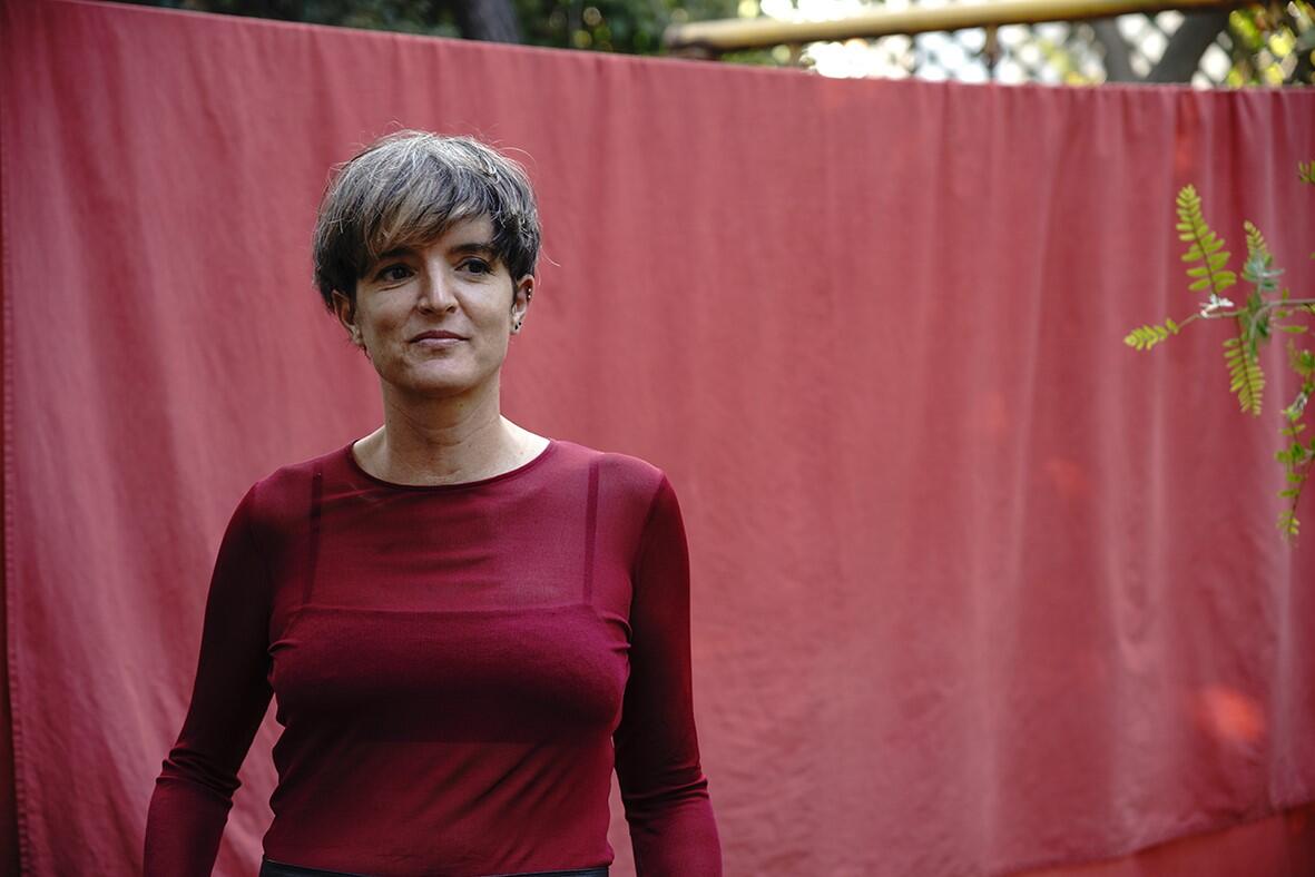 Woman with short hair wearing maroon shirt in front of red curtain